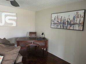 A room with a wooden desk, a chair, a lamp, and a large cityscape painting on the wall. - The Sunshine Sanctuary 
Entire home Private Pool & 2 Bedroom and 2 FullBathrooms (Sarasota)