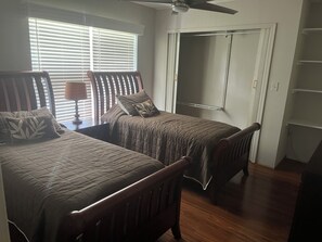 Un dormitorio con dos camas, ventilador de techo, ventana con persianas y armario.