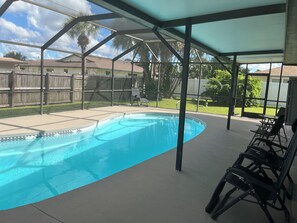 A covered outdoor swimming pool with a patio area, surrounded by a wooden fence and palm trees. - The Sunshine Sanctuary 
Entire home Private Pool & 2 Bedroom and 2 FullBathrooms (Sarasota)