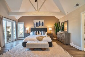 Une chambre spacieuse avec un grand lit, une commode en bois et un balcon agrémenté de rideaux.