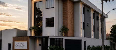 A modern two-story building with a flat roof, large windows, and a sign indicating it is a residential property.