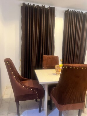 A dining area with a white table, two brown chairs with gold studs, and dark curtains. - Perfect 2-bedroom apartment in Akure for a relaxing stay (Akure)