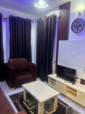 A living room with a sofa, a TV on a stand, a white coffee table, and curtains. - Perfect 2-bedroom apartment in Akure for a relaxing stay (Akure)