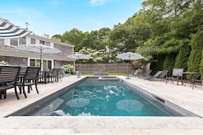 A rectangular swimming pool with a clear blue water surface, surrounded by a patio area with lounge chairs and umbrellas. - Expansive Cape Cod Family Retreat (Osterville)