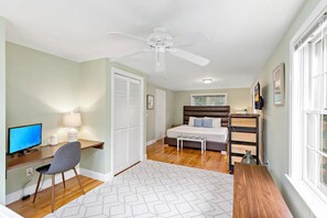 A bedroom with a bed, bedside table, lamp, desk with computer, chair, and a ceiling fan. - Expansive Cape Cod Family Retreat (Osterville)