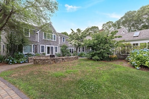A residential property with a stone retaining wall, a grassy lawn, and mature trees. - Expansive Cape Cod Family Retreat (Osterville)