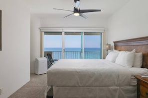 A hotel room with a bed, a ceiling fan, a view of the sea through a balcony door, and a small table with a lamp. - Sunsets on the Shoreline | Oceanfront Kona Home (Kailua-Kona)