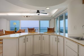 A modern kitchen with a central island, white cabinetry, and a view of the ocean. - Sunsets on the Shoreline | Oceanfront Kona Home (Kailua-Kona)