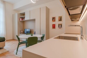 A modern kitchen with a white countertop, a stainless steel sink, and a dining area with a white table and green chairs. - Benny Suite is a renovated studio apartment at Via Alfieri 16b, in the heart of Turin.Elegant, bright, and meticulously detailed, it combines modern design and comfort.You'll find a cozy living/sleeping area, a fully equipped kitchenette, and a bathroom  (Turin)