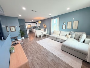 A modern living room with a grey sofa, a dining table, and a kitchen in the background. - Charming 10 acre homestead stay in Ennis (Ennis)