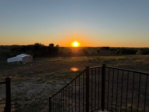 A sunset over a field with a fenced area and a small structure. - Charming 10 acre homestead stay in Ennis (Ennis)