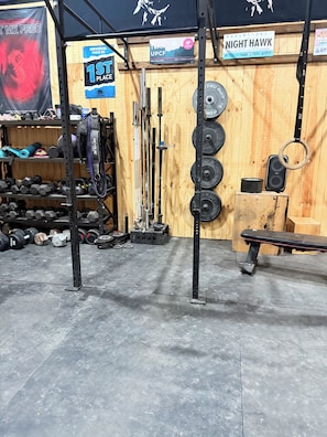 A gym with weightlifting equipment, a bench, and a wooden wall with various signs. - Charming 10 acre homestead stay in Ennis (Ennis)