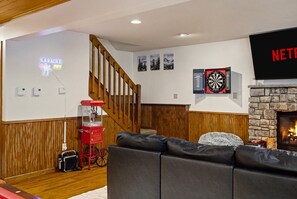 A living room with a fireplace, a red popcorn machine, a dartboard, and a TV mounted on the wall. - Poconos Retreat: Sauna, Hot Tub, Fire Pit & Games (Lake Harmony)