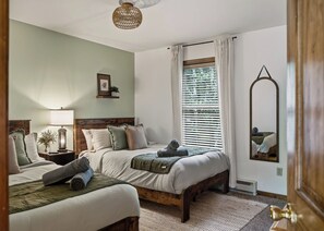 A bedroom with two beds, a bedside table with a lamp, a window with blinds, and a mirror on the wall. - Poconos Retreat: Sauna, Hot Tub, Fire Pit & Games (Lake Harmony)