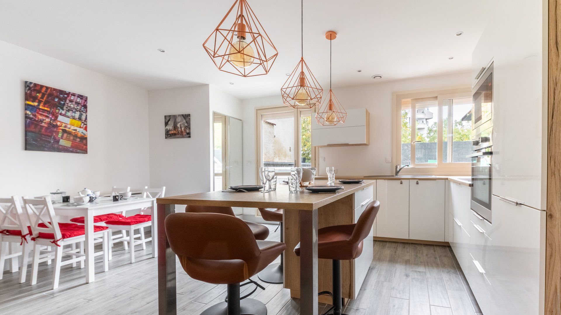 Une cuisine moderne avec des meubles blancs, un plan de travail en bois et des luminaires suspendus.