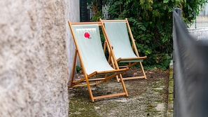 Two wooden lounge chairs with canvas seats, positioned outdoors with a stone wall and greenery in the background. - L’Île Verte – Auditorium – Exhibition Centre (Dijon)