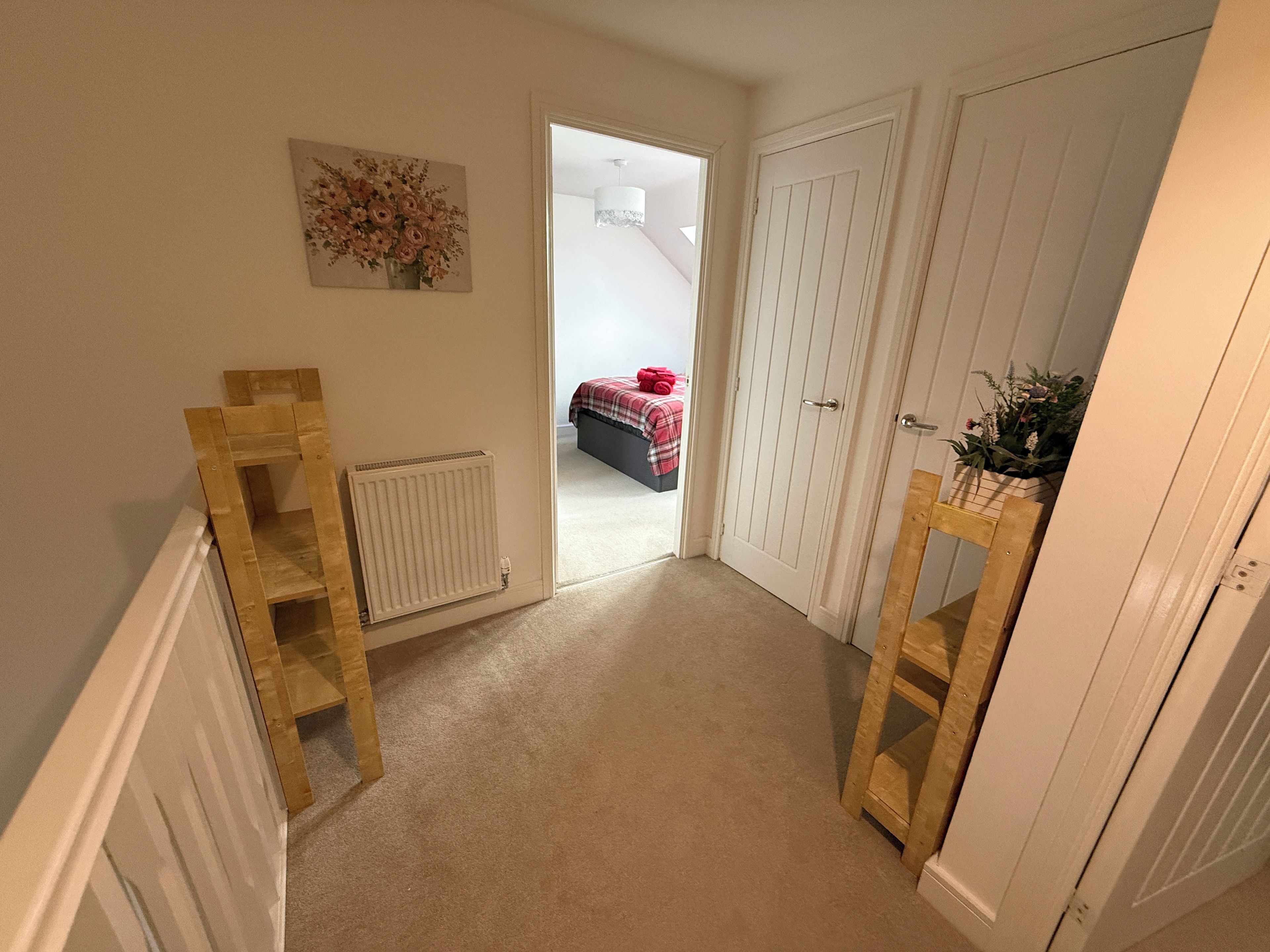 A hallway with a radiator, a wooden chair, a potted plant, and a door leading to a bedroom with a bed and a red blanket.