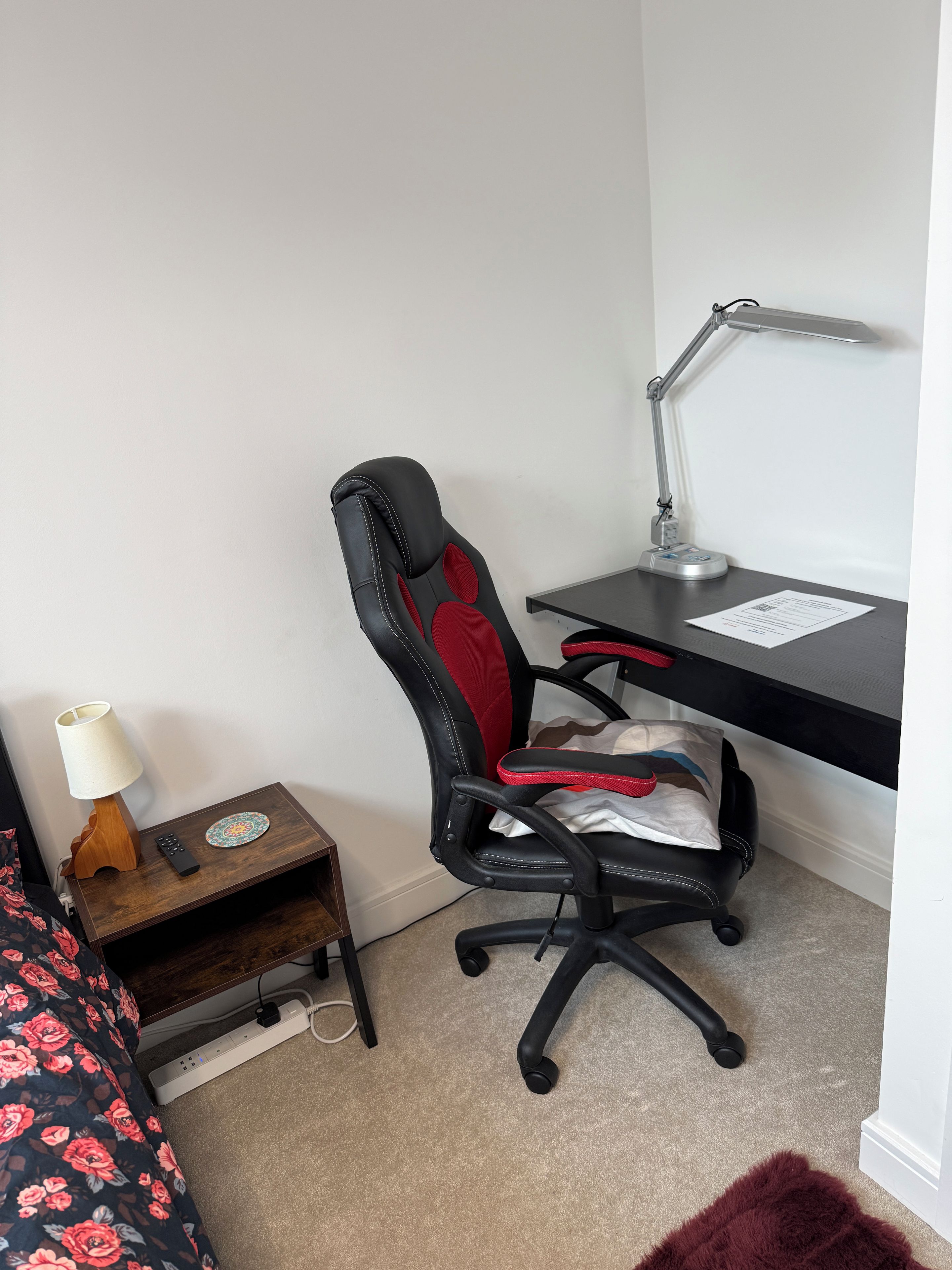 A room with a desk, a chair, a lamp, a remote control, and a power strip.