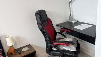 A room with a desk, a chair, a lamp, a remote control, and a power strip.