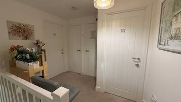 A hallway with a staircase, a door with a number, and a floral arrangement on a shelf.