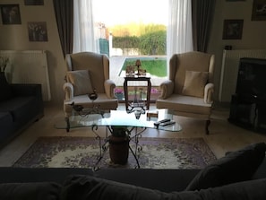 Una sala de estar con una mesa de centro de vidrio, dos sillones, un sofá, un televisor y vista a una piscina.