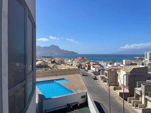 A residential area with a swimming pool, a view of the sea, and a mountain in the distance. - Adorable 2-bedroom apartment in vibrant Mindelo perfect for relaxing stay (Mindelo)