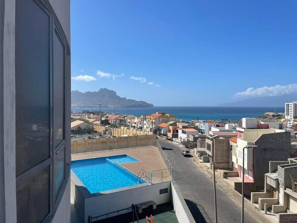 Un quartier résidentiel doté d’une piscine, offrant une vue sur la mer et sur une montagne située au loin.