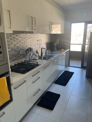 A modern kitchen with white cabinets, a gas stove, and a large window. - Adorable 2-bedroom apartment in vibrant Mindelo perfect for relaxing stay (Mindelo)