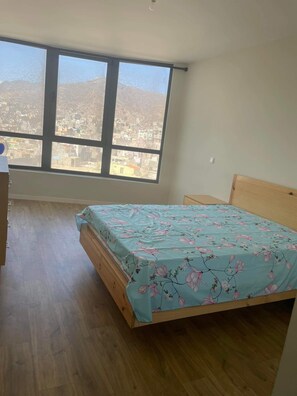 Une chambre dotée d’une grande fenêtre, d’un plancher en bois et d’un lit recouvert d’une couvre-lit à motifs floraux.