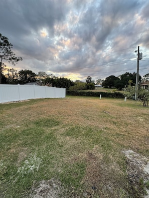 A grassy outdoor area with a white fence, trees, and a utility pole. - Beautiful House in Sebring! Sleeps 8 (Sebring)