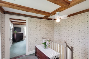 Ein Zimmer mit Holzboden, einem weißen Deckenventilator, einem Bett mit weißer Bettdecke und einer Blumenvase, sowie einem Wandpapier mit Muster.