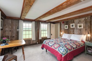 Un dormitorio con techo de madera, una cama con colcha, un escritorio con silla y una ventana con cortinas.