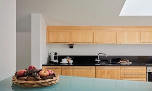 Una cocina moderna con armarios de madera, encimera negra y una mesa de vidrio con frutero.