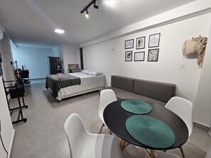 Ett modernt och väl upplyst rum med en säng, en soffa och en matplats med ett bord och stolar.