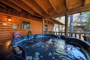 Ein Whirlpool in einer Holzhütte mit einer Holzdiele und Blick auf Bäume.