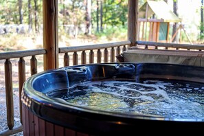 A hot tub in an outdoor setting with a wooden deck and a tent in the background. - Southern Grace: Hot Tub, Fire Pit & Walkable Location (Broken Bow)