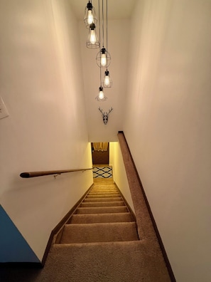 A staircase with carpeted steps, a wooden handrail, and a wall-mounted deer head decoration.