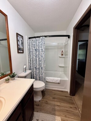Ein Badezimmer mit Toilette, Waschbecken, Spiegel, Dusche und Handtuchhalter.