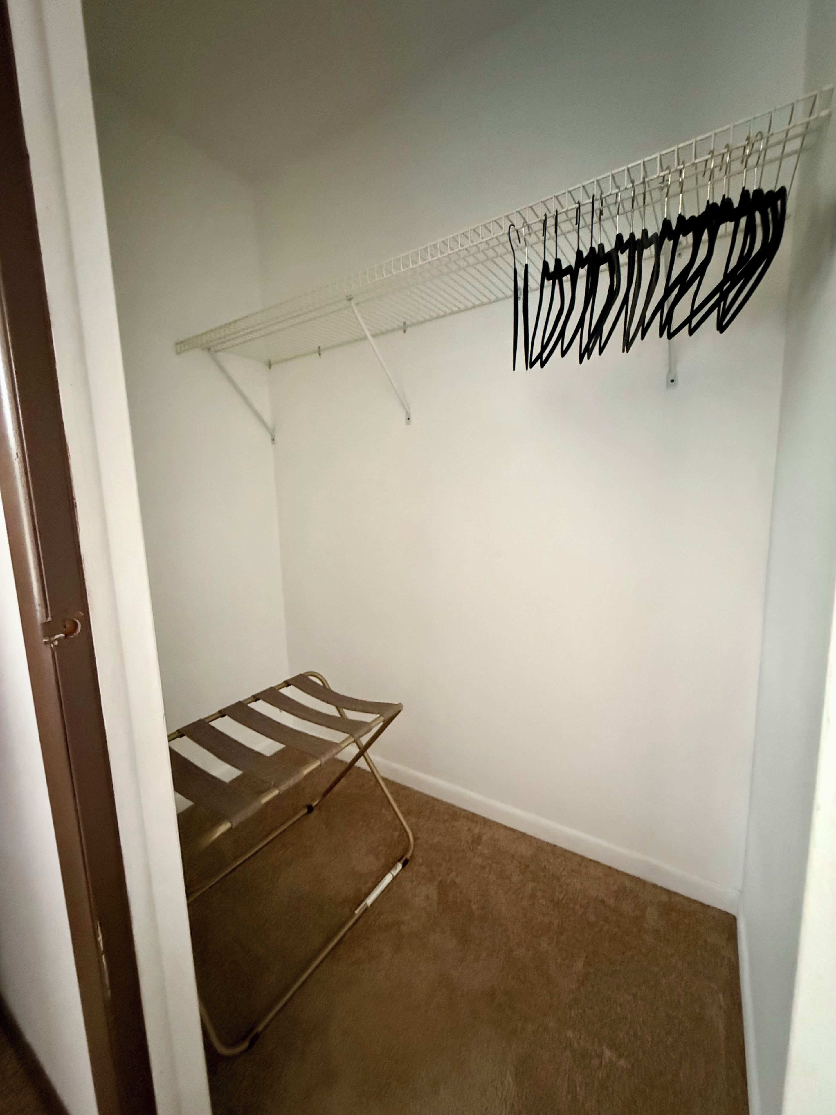 Un armario de entrada con un tendedero metálico y una silla plegable.