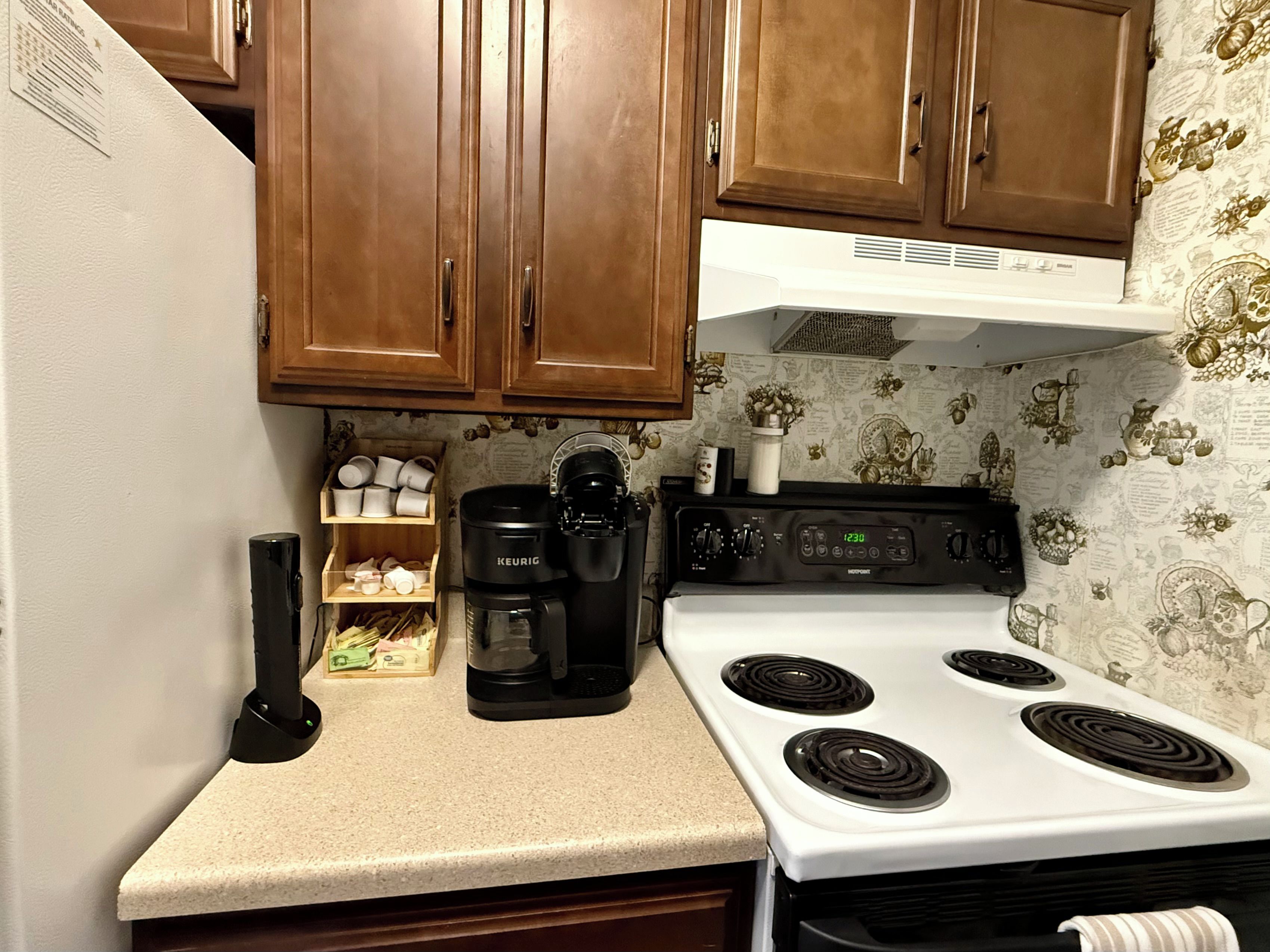 Une cuisine avec des meubles de rangement en bois, un fourneau blanc, une machine à café et une étagère avec des tasses.