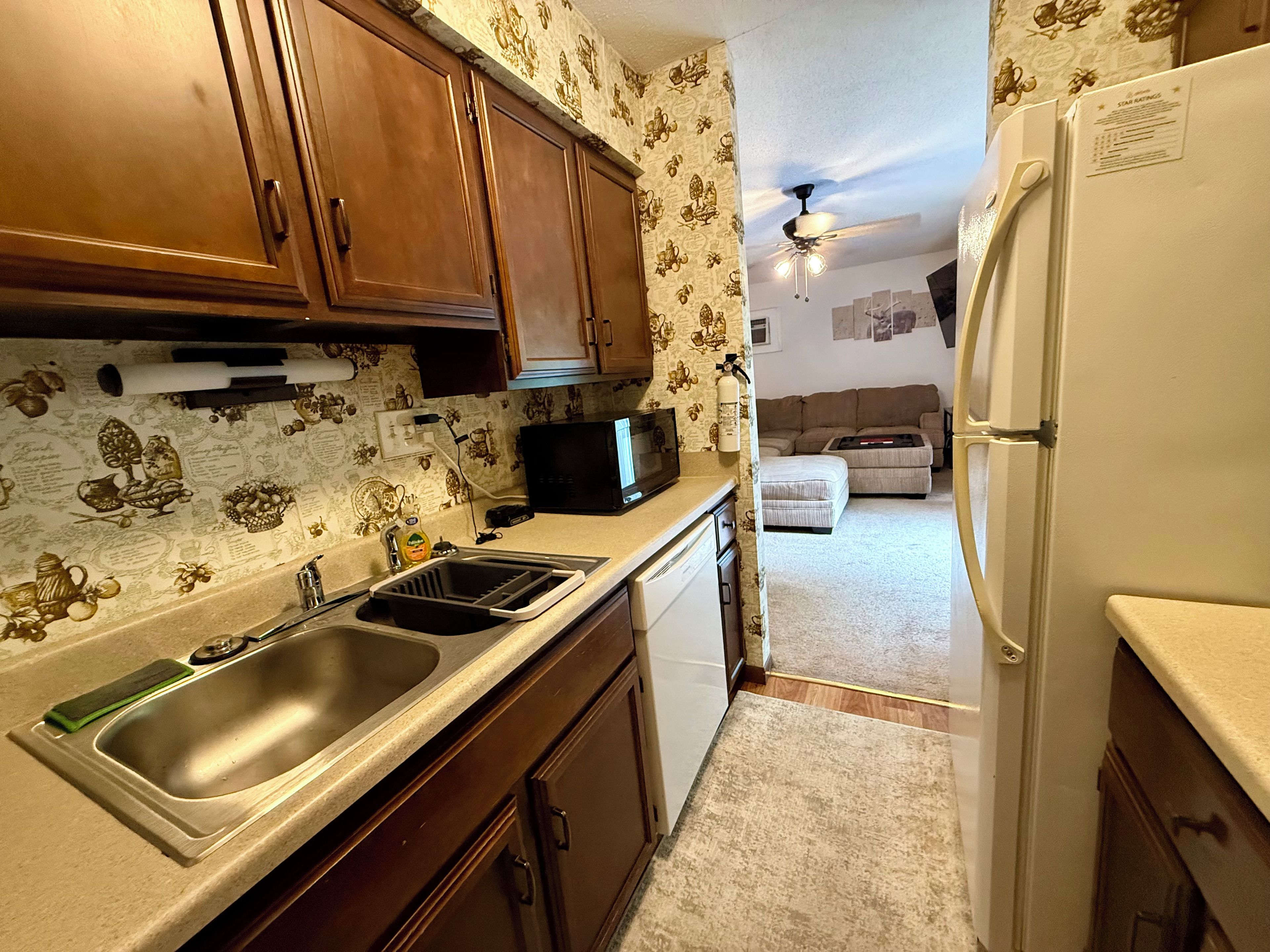 A kitchen with wooden cabinets, a stainless steel sink, a microwave, and a refrigerator.