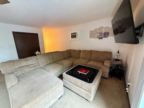 Una sala de estar con un sofá modular, una mesa de centro, un televisor y una mesita auxiliar con una lámpara.