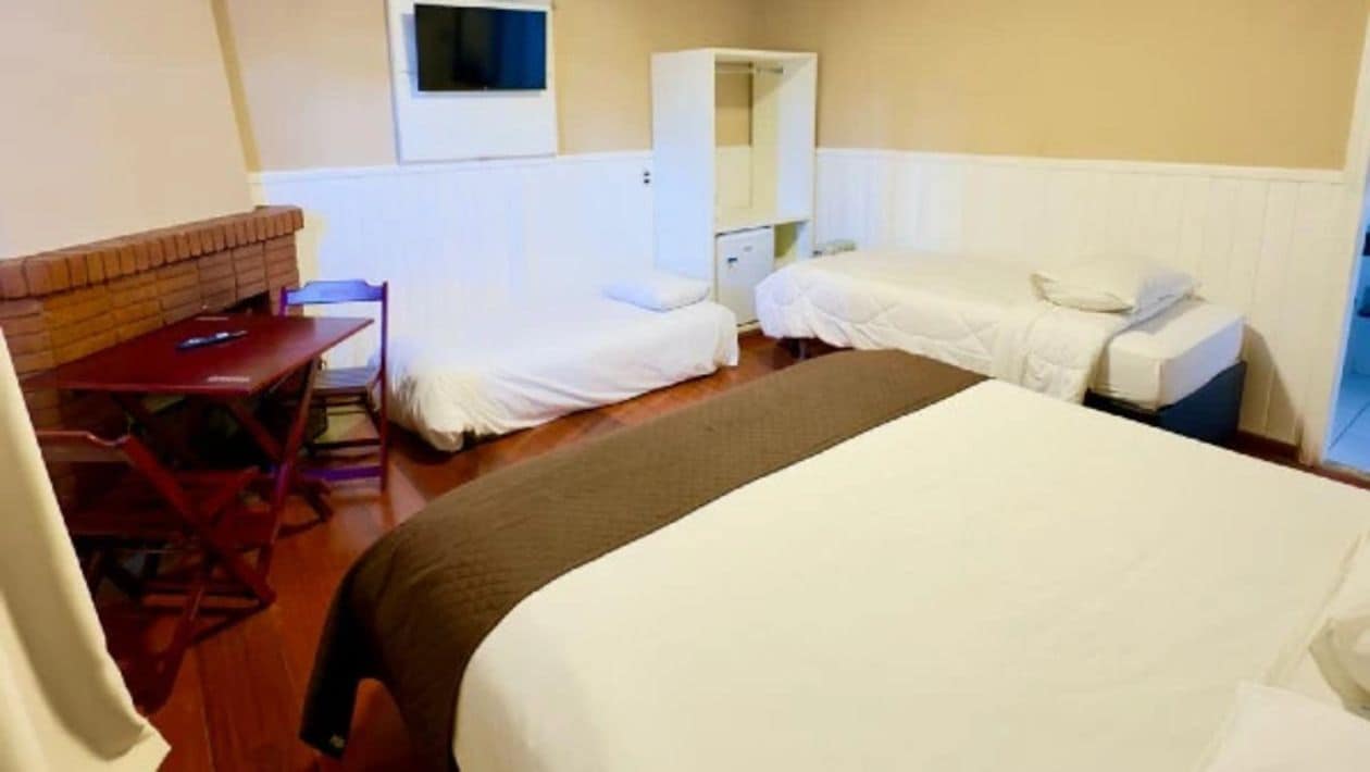 Una habitación con una cama grande, un escritorio, dos camas individuales, un armario y un televisor en la pared.