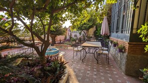 Une terrasse extérieure avec une table et des chaises, entourée de plantes en pot et d’une fontaine.