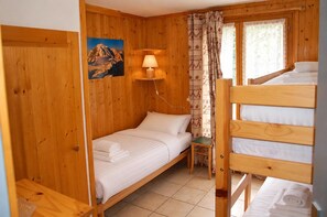 A wooden cabin room with a bed, a small table, a lamp, and a painting of a mountain. - New Listing (Chamonix-Mont-Blanc)
