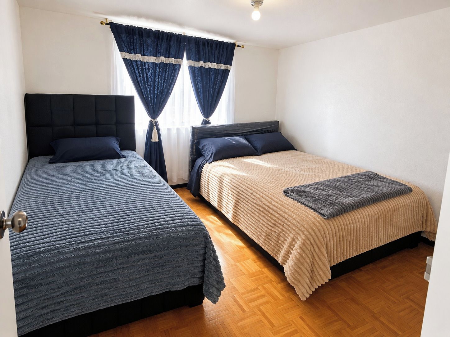 Una habitación con dos camas, una ventana con cortinas y una lámpara.