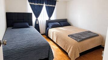 Una habitación con dos camas, una ventana con cortinas y una lámpara.