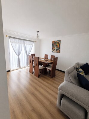 Un comedor con una mesa y sillas de madera, un sofá y una ventana con cortinas translúcidas.