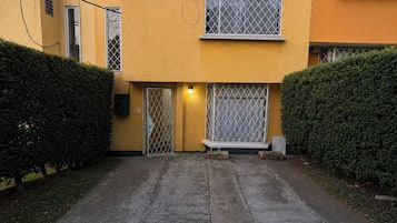 Edificio de dos pisos con entrada protegida por una reja, un ventanal pequeño con reja de metal y una lámpara sobre la puerta.