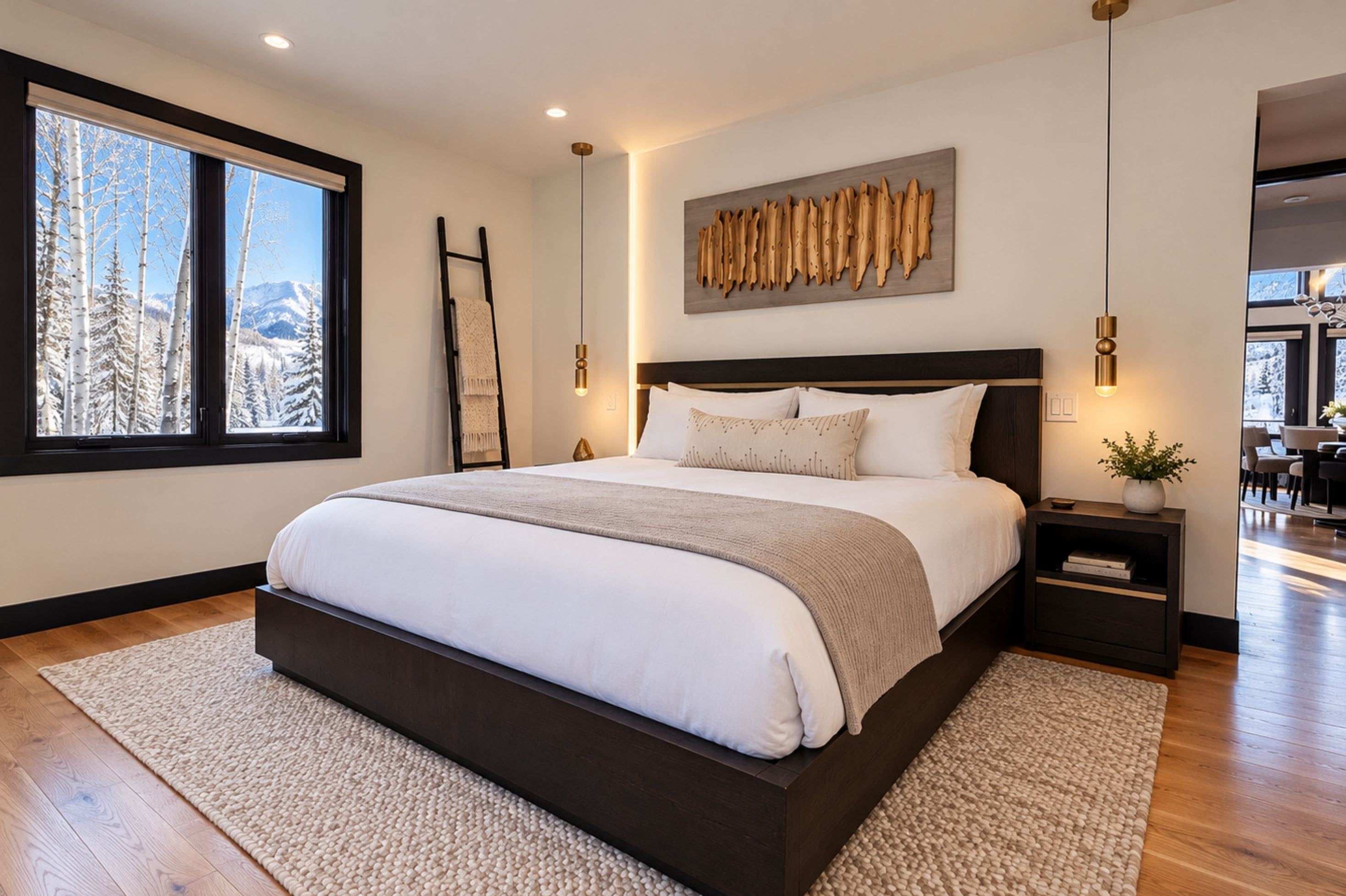 A modern bedroom with a large bed, a view of trees through a window, and a wooden wall art piece.